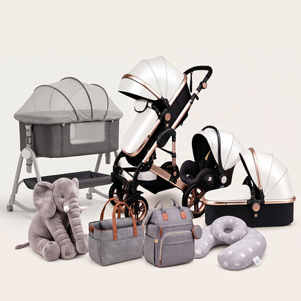 A baby travel system and nursery accessory set arranged on a light beige studio background. The set includes a bassinet, stroller, infant car seat with canopy, bassinet cover, plush elephant toy, diaper bags, and a travel pillow.